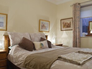 A neatly made bed with a beige blanket and pillows, a bedside table with a lamp, and framed pictures on the wall.