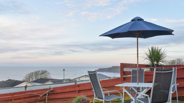 A patio with a table and chairs, a blue umbrella, and a view of the sea. - 2 bedroom accommodation in Knipe Point, near Cayton (Knipe Point, near Cayton)