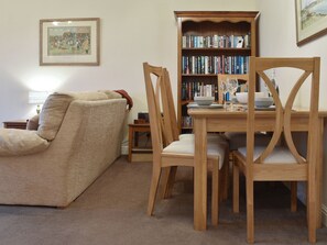 A living room with a sofa, wooden dining table, chairs, a bookshelf, and a lamp.