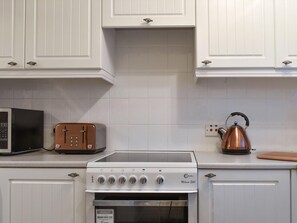 A kitchen with white cabinets, a microwave, a toaster, a kettle, and a stove.