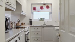 A compact kitchen with white cabinetry, a built-in oven, a microwave, and a window with a flower decoration. - 2 bedroom accommodation in Knipe Point, near Cayton (Knipe Point, near Cayton)
