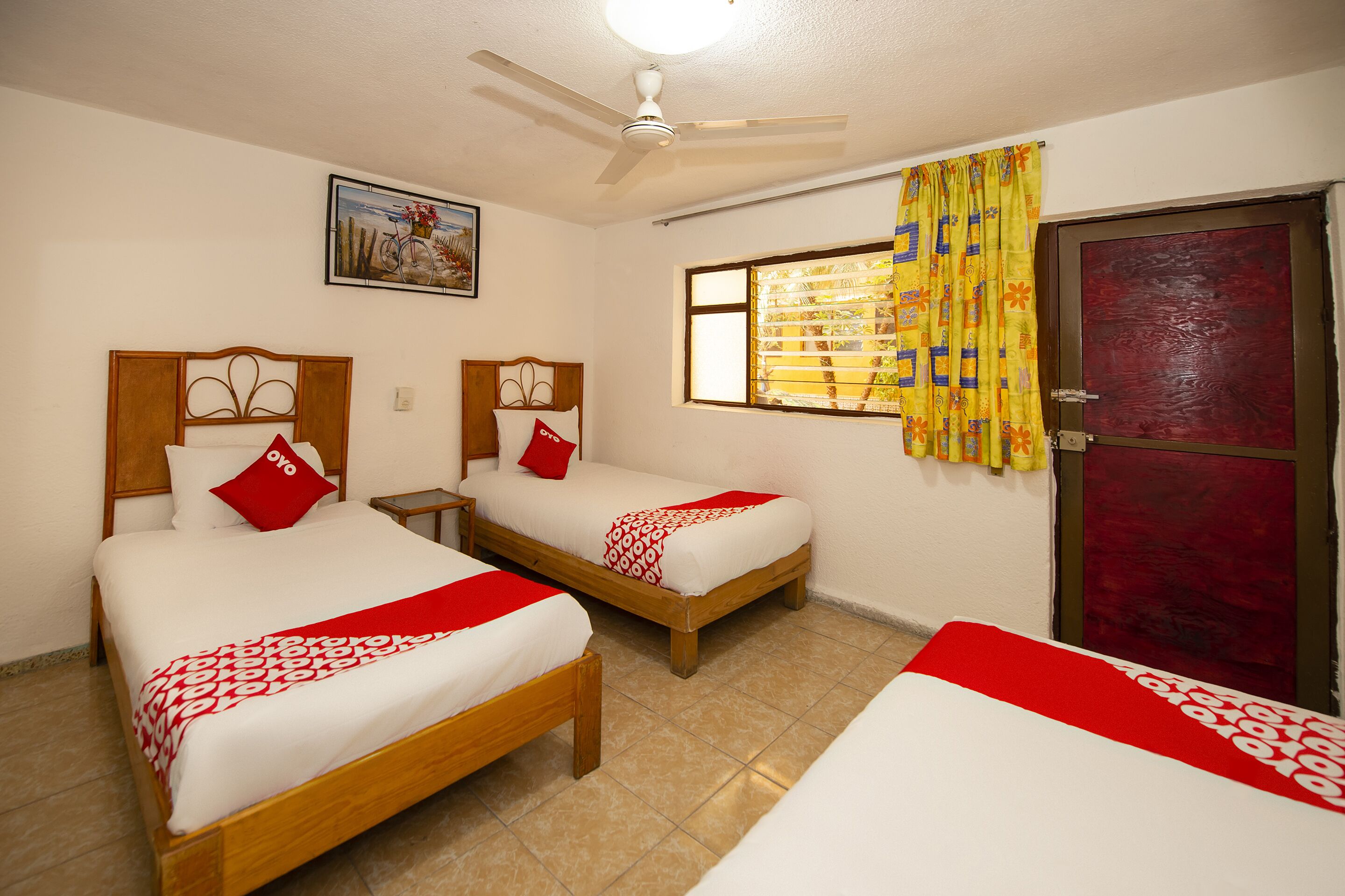 Habitación de hotel con dos camas, un ventilador de techo, una ventana con cortinas y una puerta.