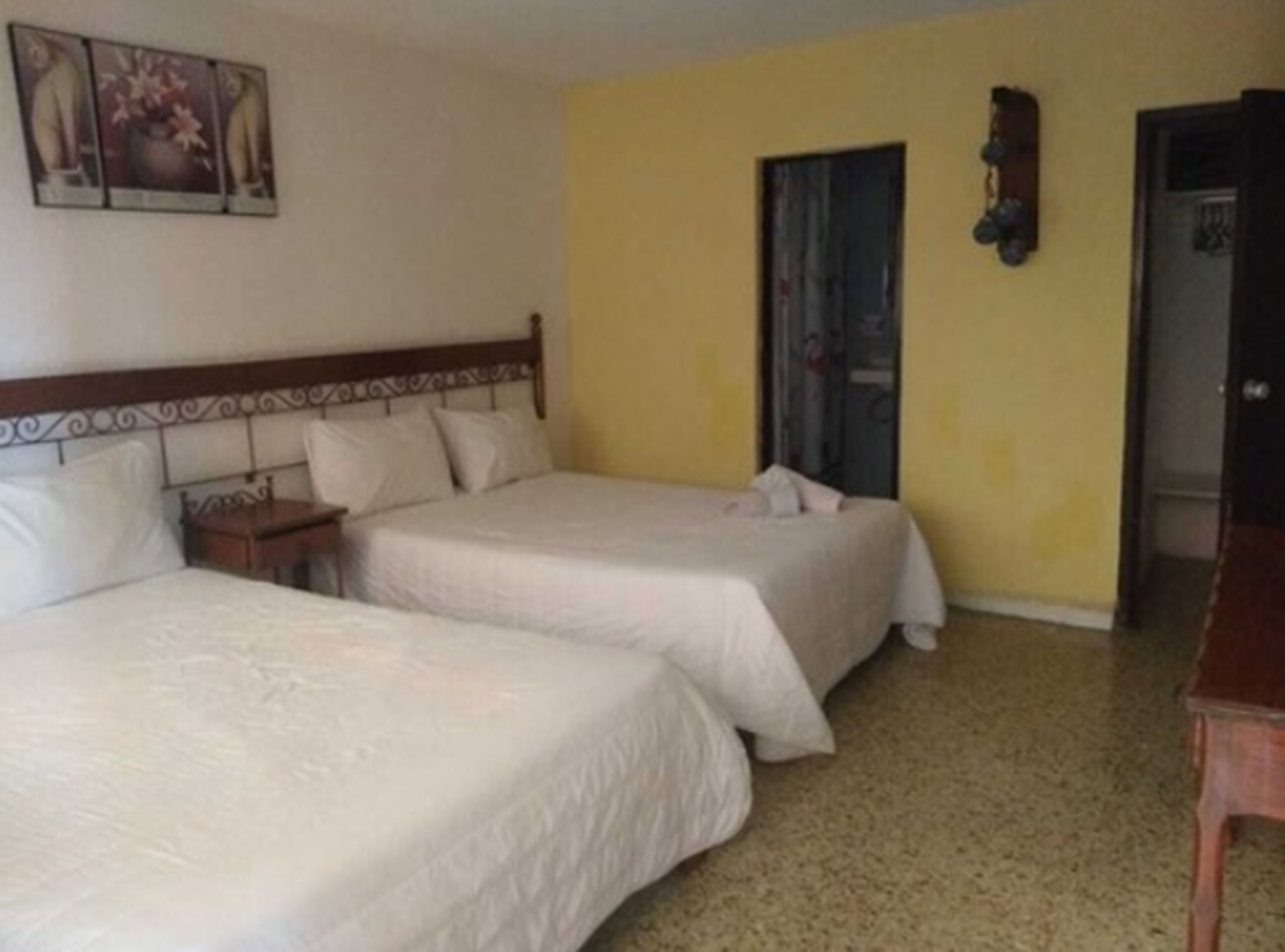 A room with two beds, a wooden headboard, a nightstand, a wall-mounted clock, and a door.