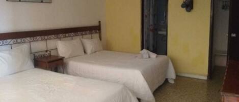 A room with two beds, a wooden headboard, a nightstand, a wall-mounted clock, and a door.