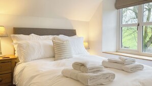 A neatly made bed with pillows and folded towels, a bedside lamp, and a window with a view of trees. - 2 bedroom accommodation in Kirkby stephen (Kirkby stephen)
