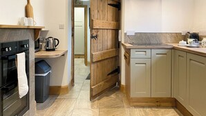 A kitchen with a wooden door, a stove, a trash bin, and a sink. - 2 bedroom accommodation in Kirkby stephen (Kirkby stephen)