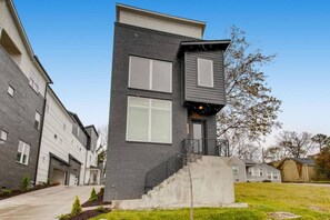 Un immeuble résidentiel moderne à deux étages, avec une façade grise, de grandes fenêtres et un petit porche à l’avant.