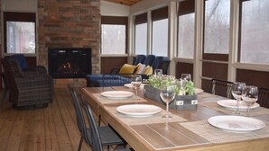 Uma sala de jantar com uma longa mesa de madeira posta para seis pessoas, lareira e um espaço de estar acolhedor com um sofá e poltronas.