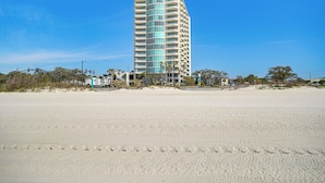 A tall, modern hotel with a curved facade, located on a sandy beach with palm trees and a clear blue sky. - Walk to Beach: Luxury Biloxi Condo w/ Pool Access! (Biloxi)