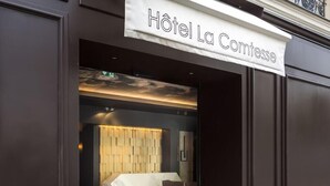 La entrada del Hotel La Comtesse con un diseño moderno, que presenta un mostrador de recepción de mármol y un cabecero de madera en el interior.