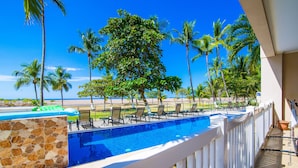 A pool area with a stone wall, lounge chairs, and palm trees. - Ocean front and just steps from the pools and ocean! (Jacó)