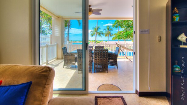 A room with a sliding glass door leading to a balcony with a view of the beach and palm trees. - Ocean front and just steps from the pools and ocean! (Jacó)