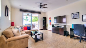 A living room with a sofa, coffee table, TV, and a ceiling fan. - Ocean front and just steps from the pools and ocean! (Jacó)