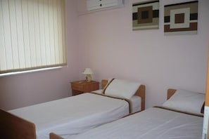 Un dormitorio con dos camas individuales, una mesita de noche con lámpara y una ventana con persianas.
