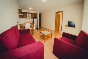 A compact living space with a kitchenette, a dining area, and a seating area with red sofas and a small table. - Marina View Fort Beach (Nessebar)