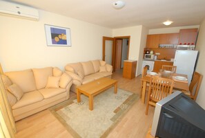 A compact living space with a sofa, a wooden coffee table, a television, a kitchen area with a microwave, and a refrigerator. - Marina View Fort Beach (Nessebar)