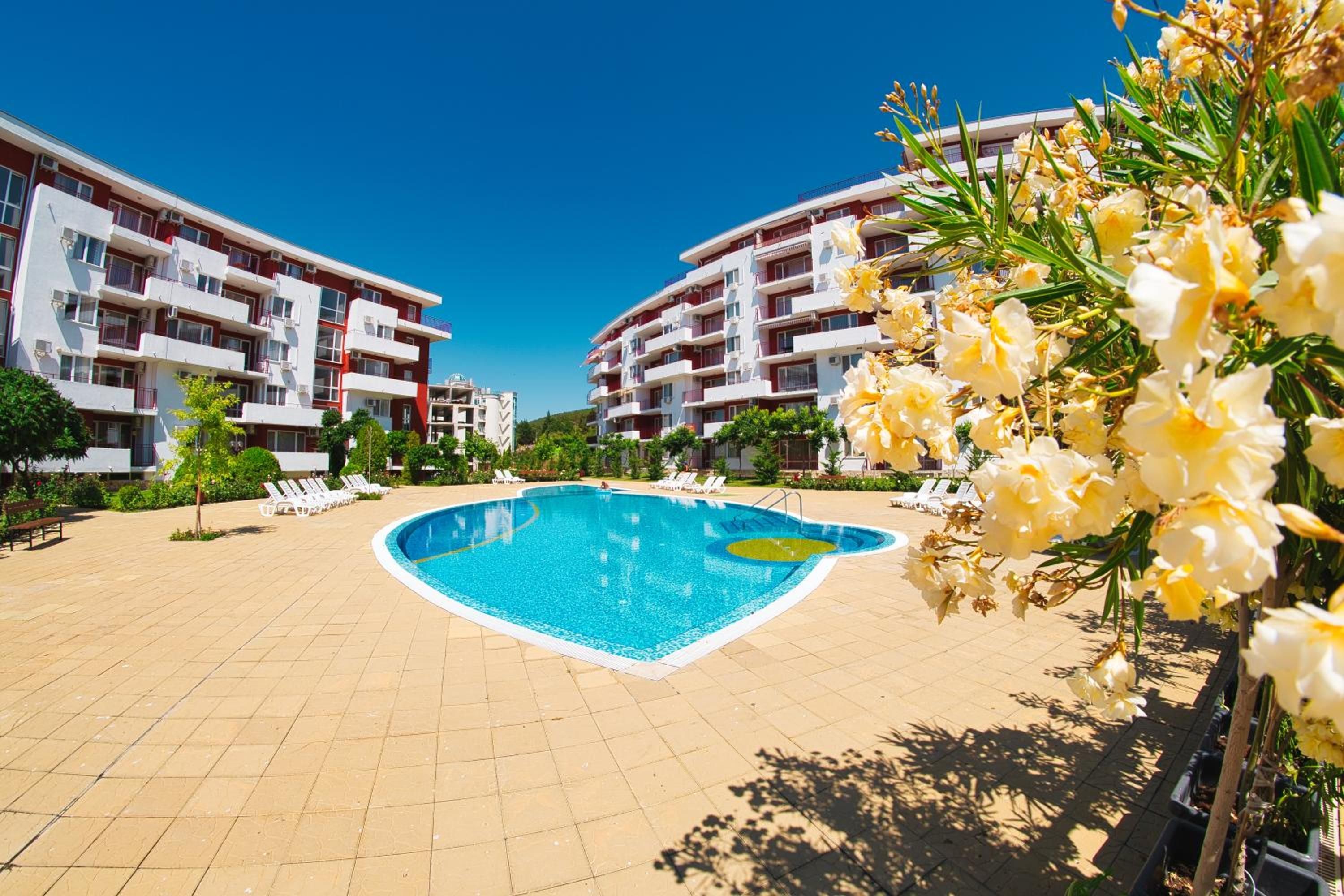 Una piscina rodeada por un solárium con sillones de descanso, con edificios de varios pisos y balcones al fondo.