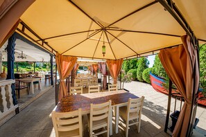 Un área de comedor al aire libre con mesas y sillas bajo una carpa grande.