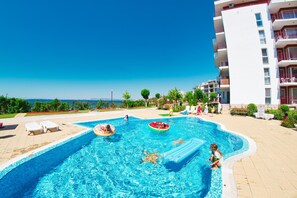 A swimming pool with a view of the sea, surrounded by a building with balconies.