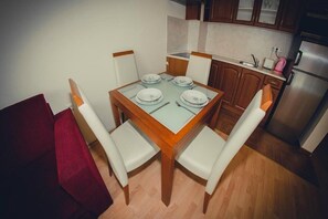 A dining area with a wooden table and four chairs, a red couch, and a kitchen in the background. - Marina View Fort Beach (Nessebar)