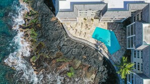An aerial view of a coastal property with a swimming pool, rocky shoreline, and modern architecture.