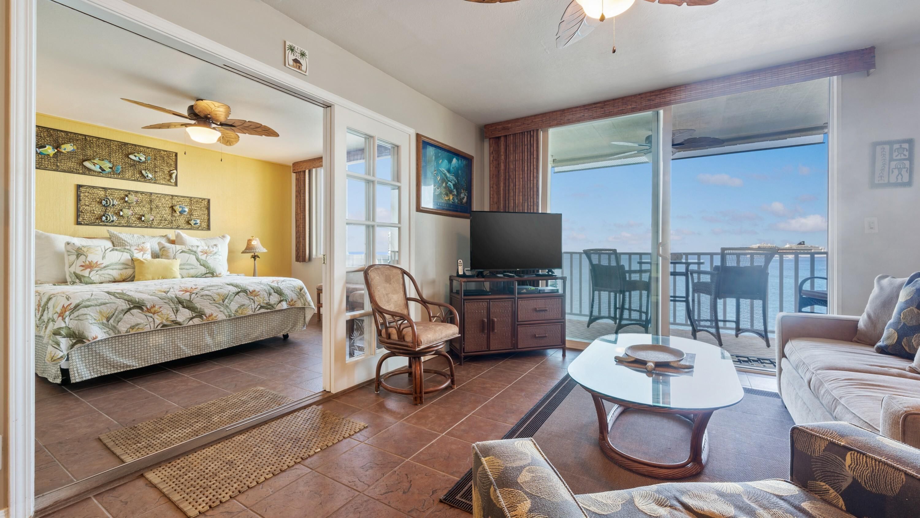 Amplia sala de estar con una cama, televisor, balcón con sillas y una mesa de comedor.