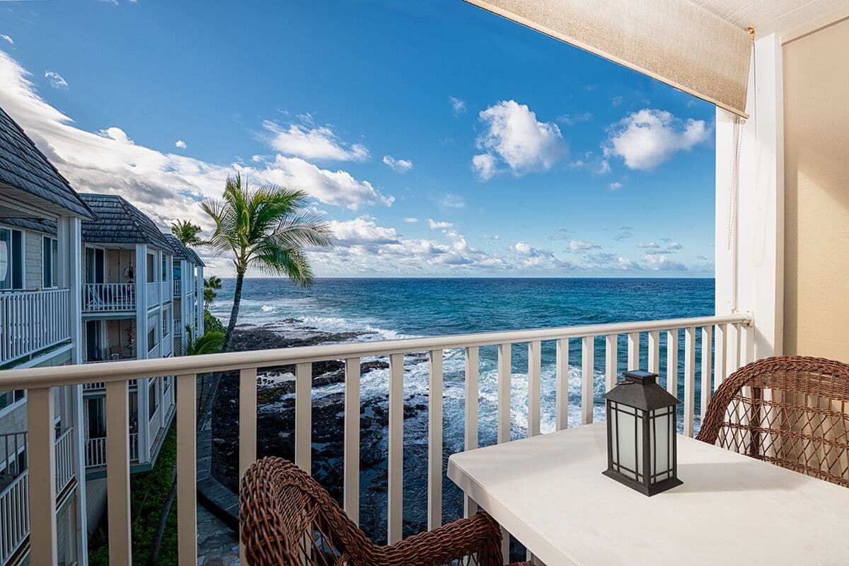 Ein Balkon mit Blick auf das Meer, ein Korbstuhl, ein Tisch und ein Laternen.