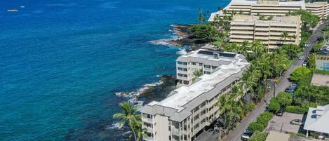 A coastal hotel with multiple balconies, a parking area, and a view of the ocean.