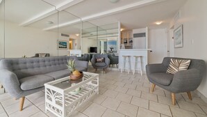 A modern living room with a grey sofa, a white coffee table, and a kitchen area in the background.