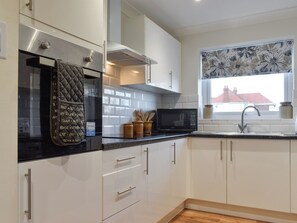 A modern kitchen with white cabinets, a black countertop, a stainless steel oven, a microwave, and a window with a floral view. - 2 bedroom accommodation in Knipe Point, near Cayton (Knipe Point, near Cayton)