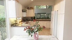 Una cocina moderna con armarios blancos, una encimera de mármol y una planta en una mesa de madera.