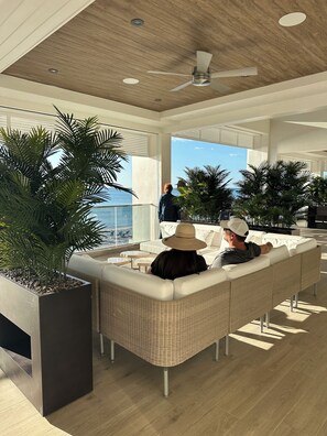 A modern lounge area with wicker furniture, large potted plants, and a view of the ocean. - Beautiful Condo with Private Beach Access and Golf Course Views (Bonita Springs)