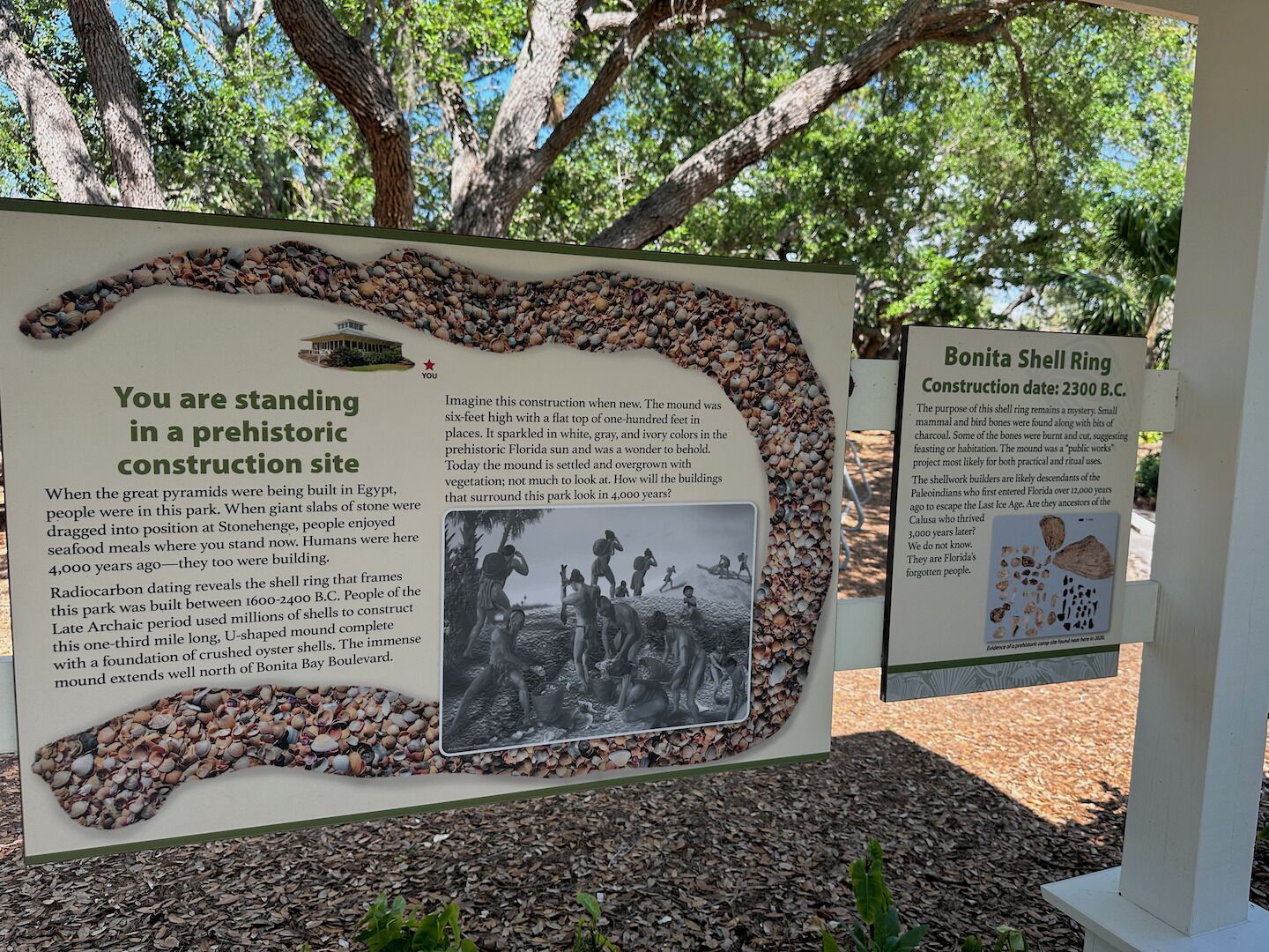A historical site with a large informational display about prehistoric construction, including a shell ring and a mound.