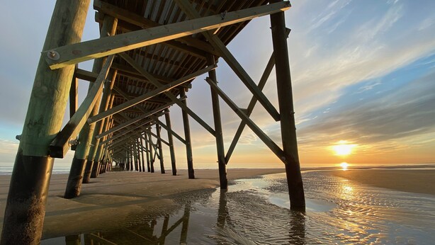 A wooden pier structure extending into calm waters with a sunset in the background.
