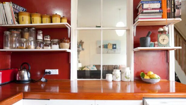 A kitchen with white cabinets, a wooden countertop, and shelves with jars, books, and kitchen utensils.