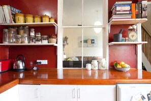Une cuisine avec des armoires blanches, un plan de travail en bois et des étagères où sont rangés des bocaux, des livres et des ustensiles de cuisine.
