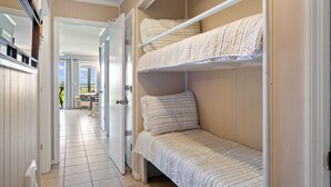 A bunk bed with striped bedding in a room with a tiled floor and a door leading to another room. - Direct Oceanfront View - Beachfront Villa (Hilton Head Island)