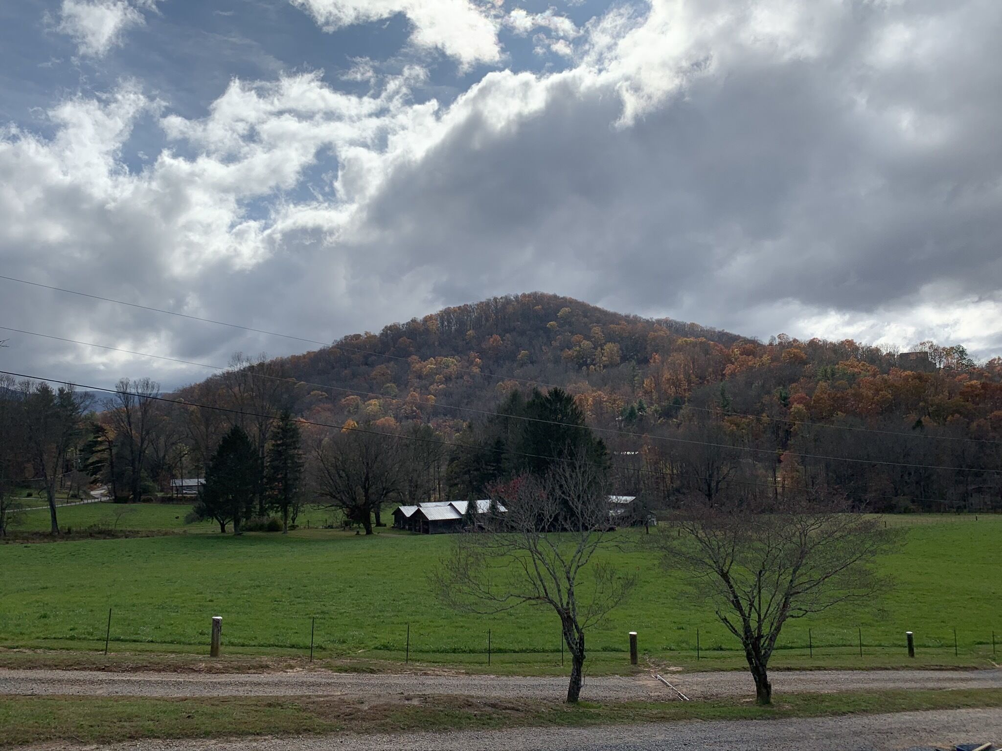 A rural landscape with a hill, trees, and a fenced field.