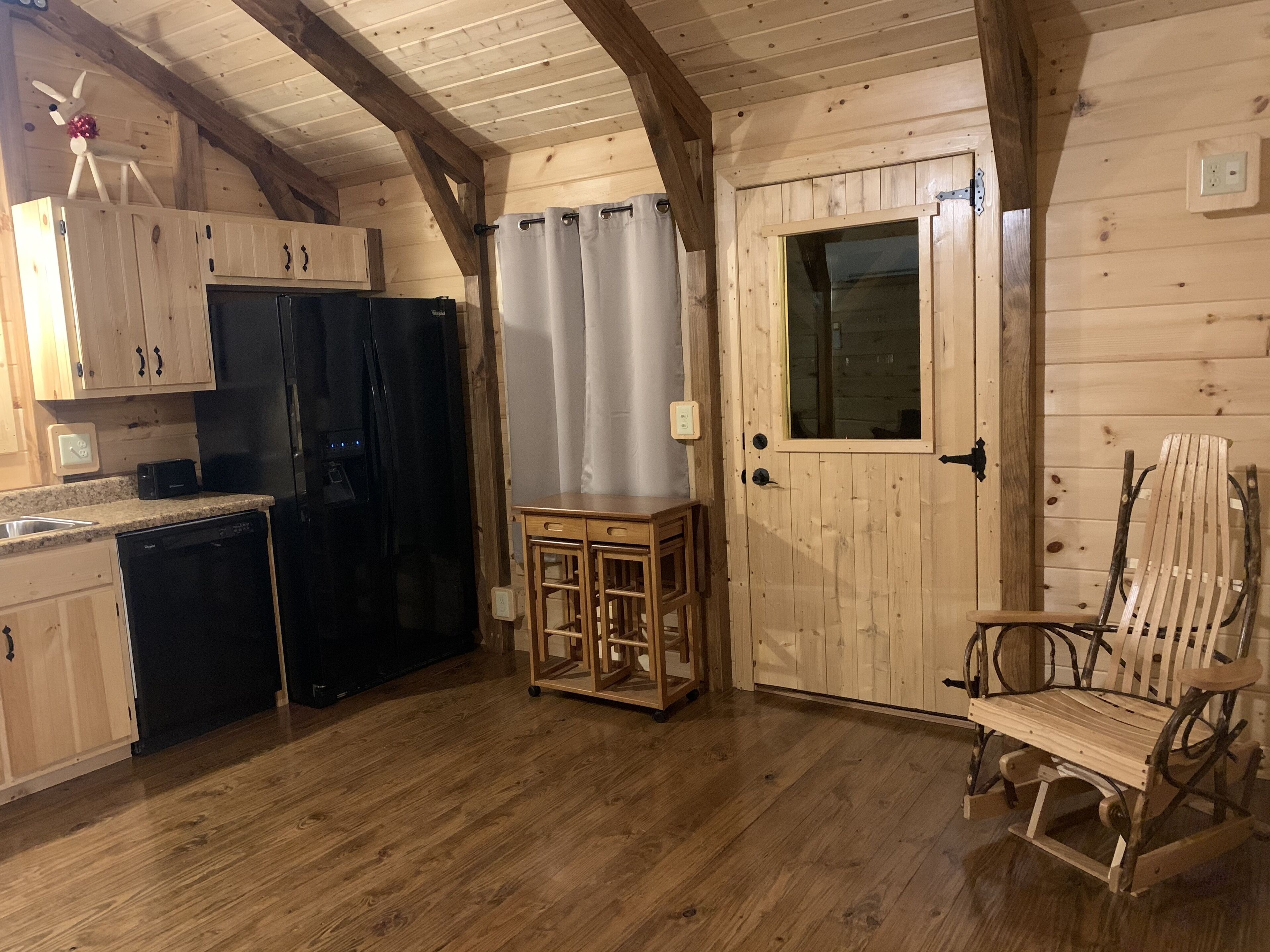 A wooden cabin interior with a kitchen area, including cabinets, a refrigerator, a wooden table, and a chair.