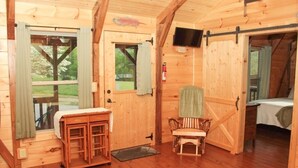 A wooden cabin with a dining area, a bench, a bed, and a TV mounted on the wall.