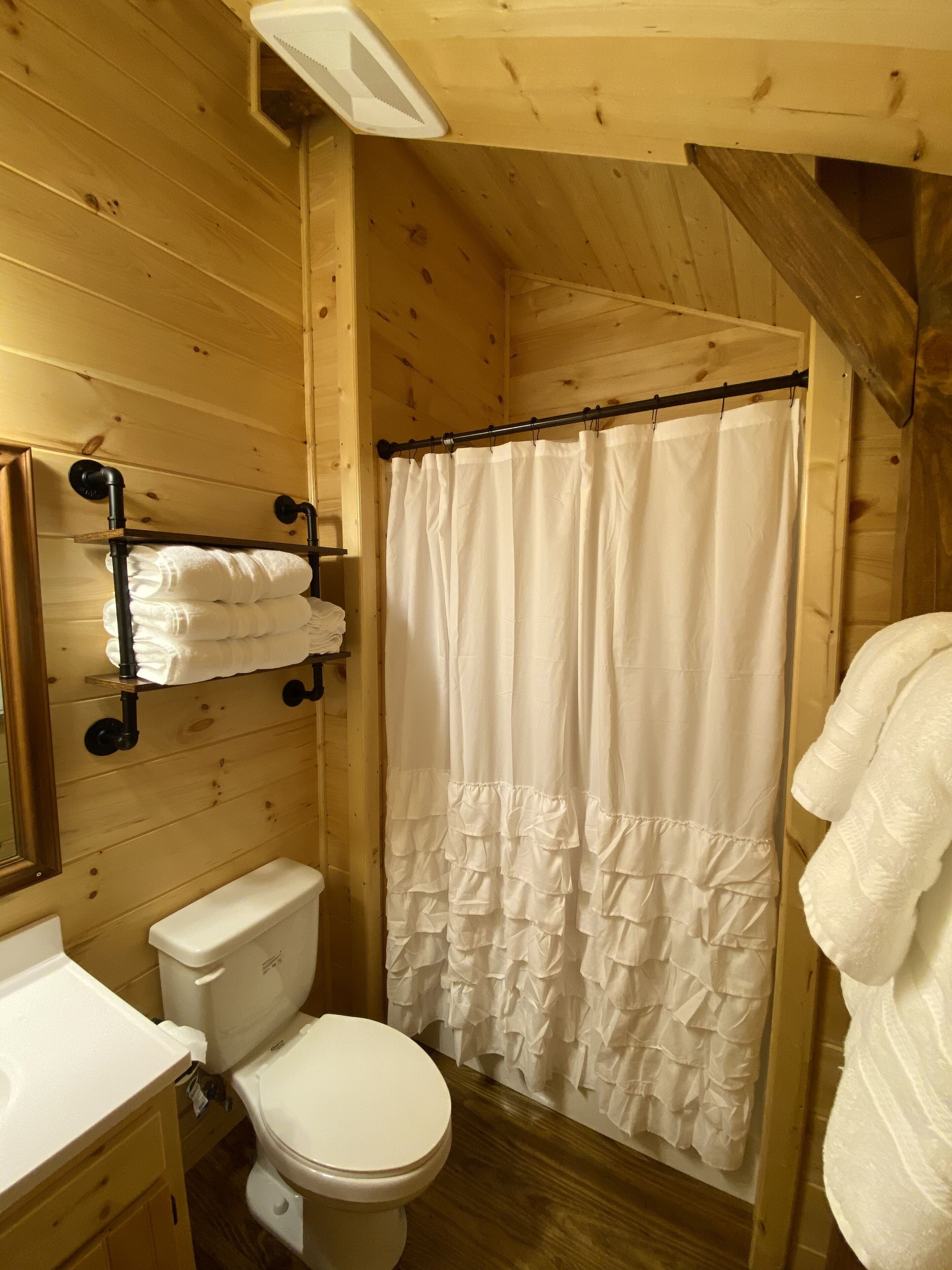 Een houten badkamer in een vakantiehuisje, met toilet, wastafel en douchegordijn.