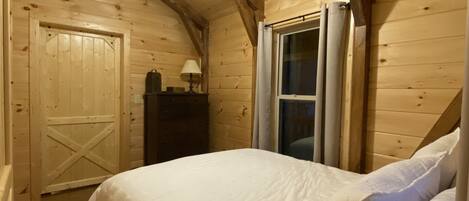 Dormitorio de cabaña de madera con cama, ventilador de techo, ventana y puerta.