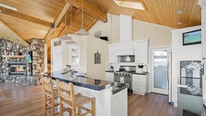 A spacious kitchen with a large island, white cabinetry, and a stone fireplace. - Pet-Friendly Retreat | Hot Tub, AC, Rec Center Access | Near Lake & Trails (Truckee)