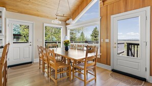 A wooden-floored dining area with a large table and chairs, large windows, and a view of a deck and trees. - Pet-Friendly Retreat | Hot Tub, AC, Rec Center Access | Near Lake & Trails (Truckee)