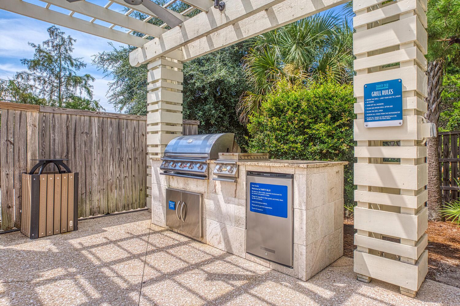 An outdoor grill area with a stone structure, a wooden fence, and a sign detailing grill rules.