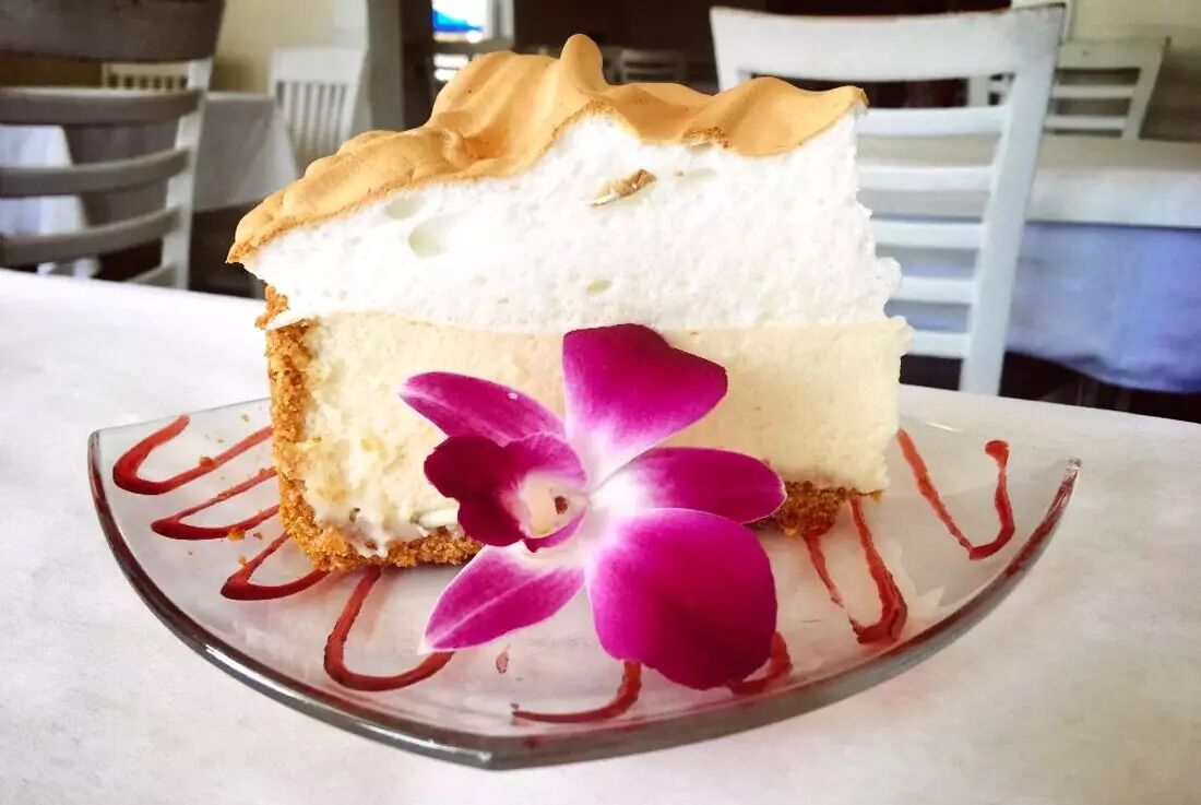 Una porción de postre en capas sobre un plato de vidrio con una decoración de orquídea púrpura.