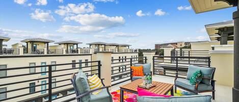Une terrasse sur le toit avec des sièges extérieurs, un tapis aux couleurs vives et une vue dégagée sur les bâtiments environnants.