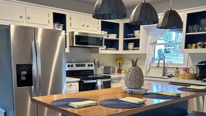 Une cuisine moderne équipée d’un réfrigérateur en acier inoxydable, d’un four à micro-ondes et d’une cuisinière. On y trouve un îlot central en bois avec des tabourets de bar et une plante en pot.