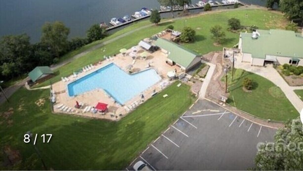 Vue aérienne d’une propriété au bord du lac, avec une piscine, un parking et un petit bâtiment.
