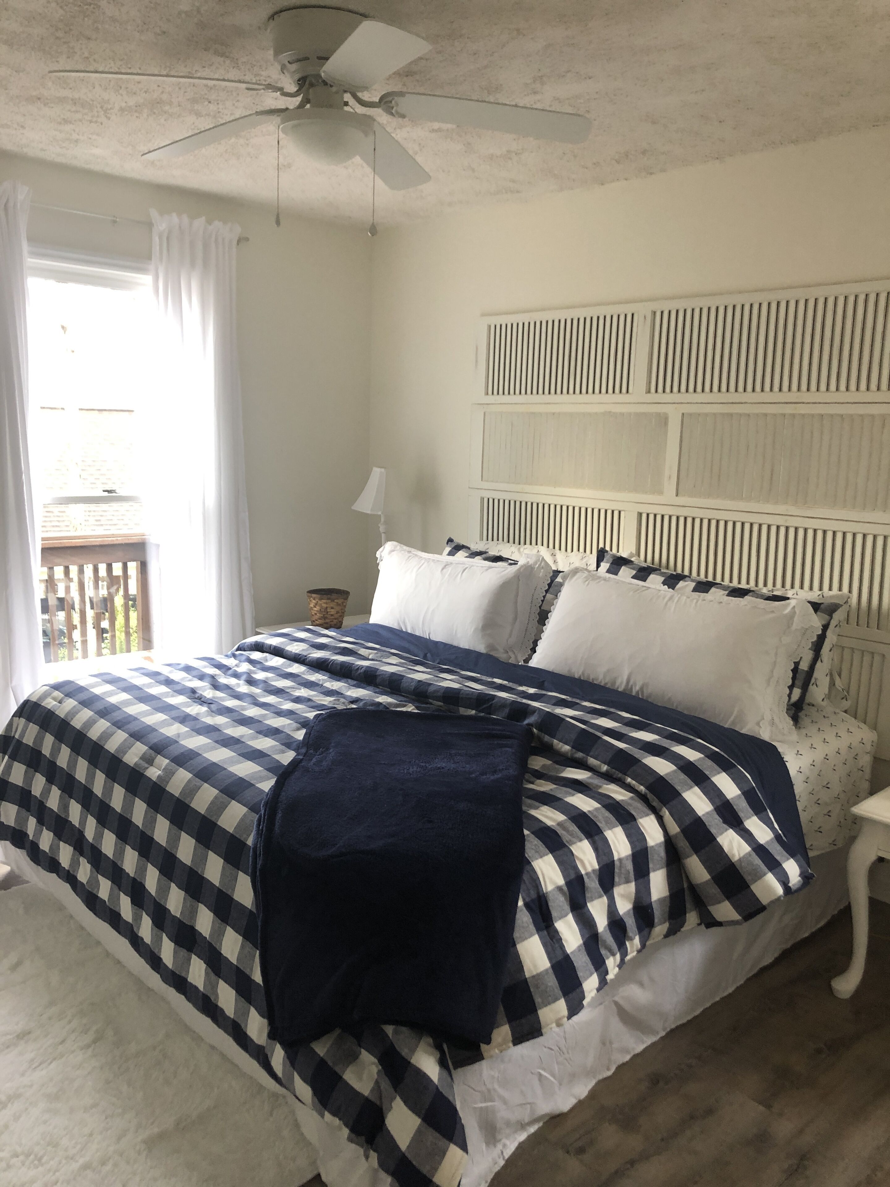 Een slaapkamer met een bed, een plafondventilator, een nachtkastje en een raam met gordijnen.